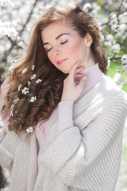 Vonzó fiatal nő göndör hajú kültéri. Gyönyörű hölgy Vértes portré a tavaszi háttér. Nő, fehér virágok a haját. Modellalkotó modell. - Fotó, kép