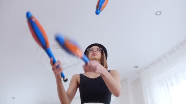 Jonge vrouw in een zwarte hoed en dragen bril jongleren in heldere studio - Video