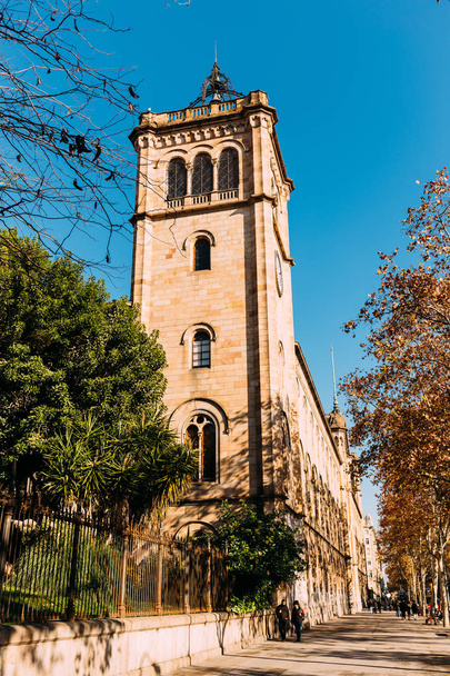 BARCELONA, SPAIN - DECEMBER 28, 2018: street with green trees and high old tower on blue sky background - Foto, Bild