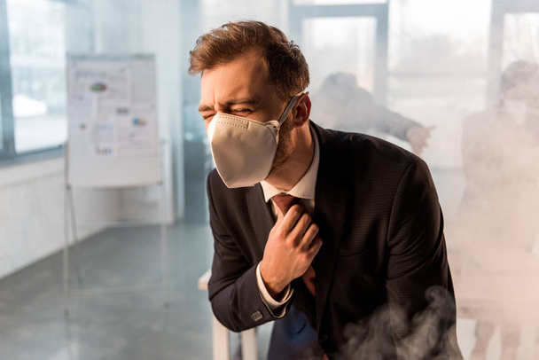 selective focus of businessman in mask standing in office with smoke near coworkers - Фото, зображення