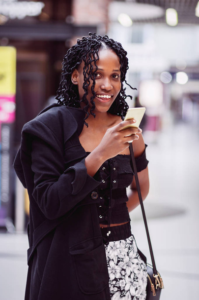 Young woman dressed in casual clothes with a phone in the hands, shopping center, soft focus background - Foto, imagen