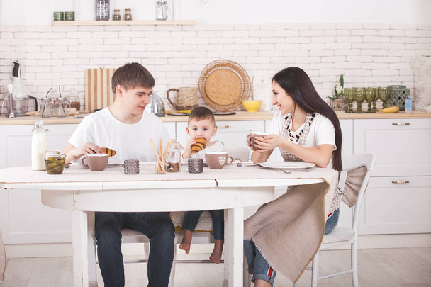 Счастливая семья завтракает вместе. Молодая семья ест за столом на кухне. Мама, папа и маленький ребенок едят
. - Фото, изображение