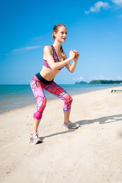 Fitness young woman working out core and glutes with bodyweight workout doing squat exercises on beach. - Photo, Image