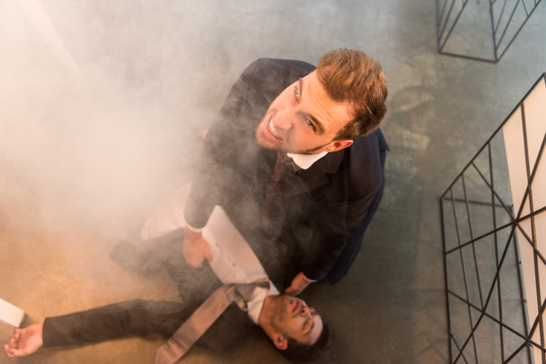 overhead view of scared businessman sitting on floor near colleague with closed eyes in office with smoke - Foto, Bild