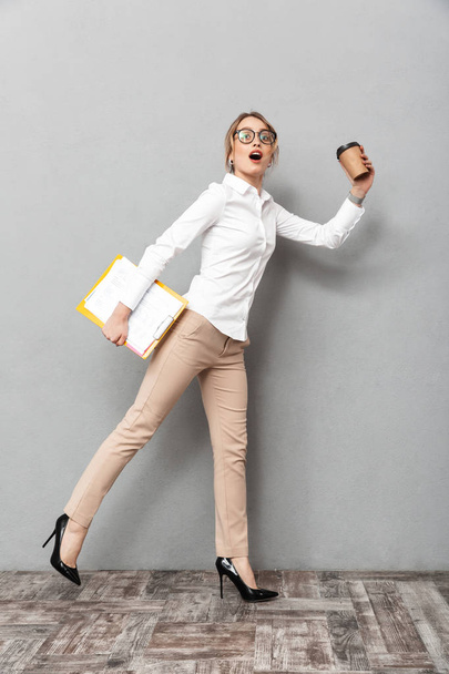 Business woman isolated over grey wall background running holding coffee and clipboard. - Фото, изображение