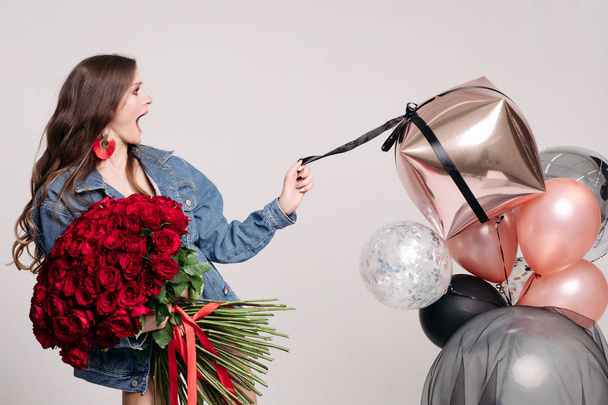 Πανέμορφο κομψό μελαχρινή γυναίκα με μάτσο αέρα μπαλόνια και κόκκινα τριαντάφυλλα. - Φωτογραφία, εικόνα
