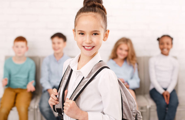 Schulmädchen trägt Rucksack mit Freunden im Hintergrund - Foto, Bild