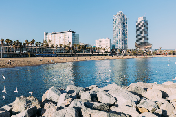 BARCELONA, SPAIN - DECEMBER 28, 2018: beautiful view of rocks, calm bay and high buildings on coast - Foto, Imagen