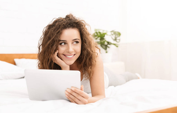 fröhliche junge Frau liegt mit Tablette im Bett - Foto, Bild