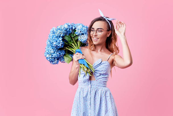 Cheerful young lady in retro round glasses being excited to get bouquet of blue spring flowers on women's day isolated over pink background. It is looking to the right, space for text - Valokuva, kuva