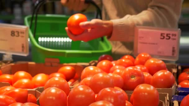 Jonge kerel kiest tomaten in een supermarkt. Een hand neemt een rode tomaat van de teller en zet het in de groene mand. Kruidenier en supermarkt. Gezonde voeding. 4 k-beeldmateriaal - Video