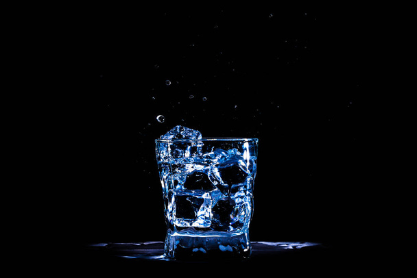 Eiswürfel fällt in ein Glas blauen Wassers oder ein Getränk auf einem schwarzen  - Foto, Bild