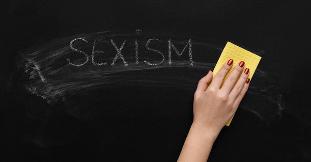 Sexismo escrito en pizarra y mano con esponja
 - Foto, imagen
