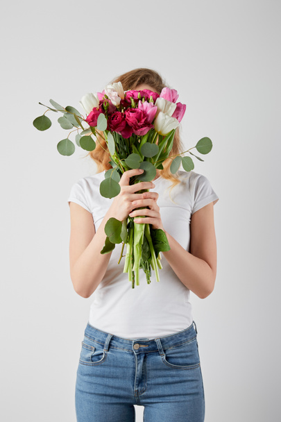 girl holding fresh bouquet with tulips, eucalyptus and roses in front of face isolated on grey - Fotografie, Obrázek