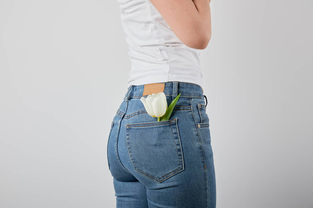 cropped view of girl with tulip flower in jeans pocket isolated on grey - Fotó, kép