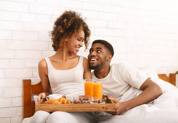 Счастливая чернокожая пара наслаждается завтраком в постели
 - Фото, изображение