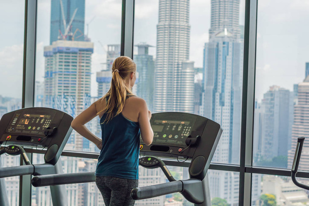 sport, fitness, lifestyle, technology and people concept - woman exercising on treadmill in gym against the background of a big city - Zdjęcie, obraz