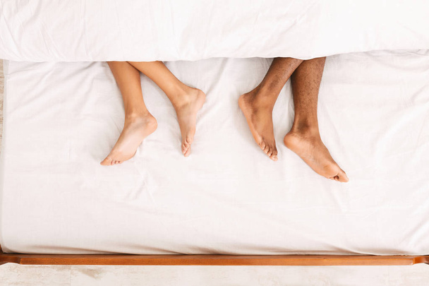 Male and female legs under duvet lying on bed - 写真・画像