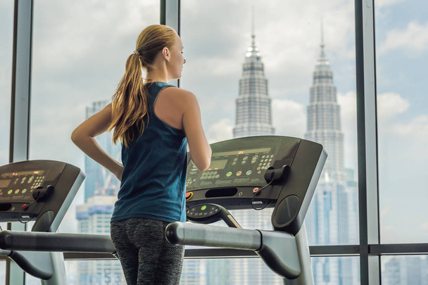 sport, fitness, lifestyle, technology and people concept - woman exercising on treadmill in gym against the background of a big city - Zdjęcie, obraz