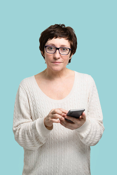 Aikuinen nainen älypuhelin kädessä katsot kameraa
 - Valokuva, kuva