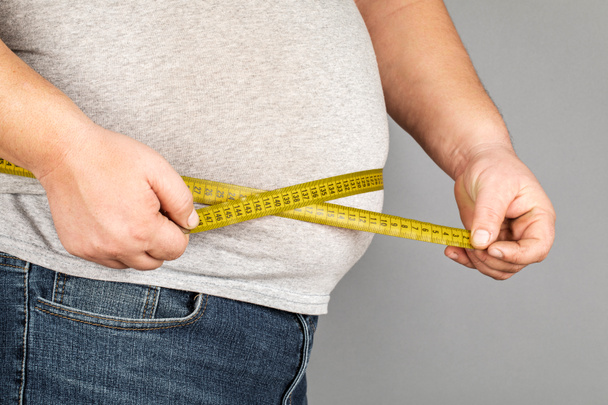 Muž měří jeho tlusté břicho měřicí páskou. šedá ba - Fotografie, Obrázek