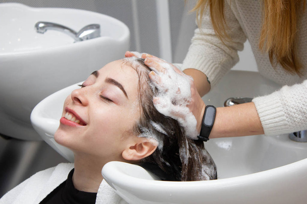 Vrouw toepassen van shampoo en masseert haar van een klant. Vrouw met haar haren gewassen in een kapsalon. - Foto, afbeelding