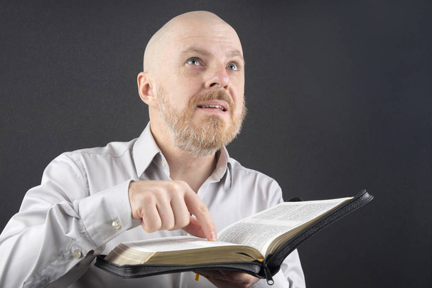 bearded man reading the Bible points his finger at the text and  - Photo, Image