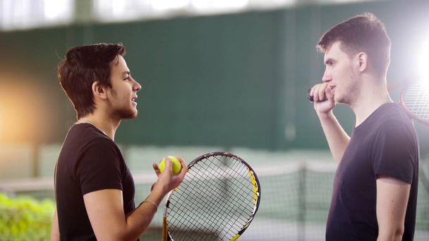 Entrenamiento en la cancha de tenis. Hombres jóvenes jugadores hablando
 - Foto, imagen