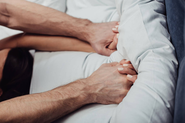 vista recortada de pareja cogida de la mano y acostada en la cama en casa
 - Foto, imagen