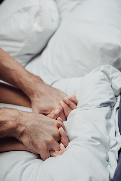 Ausgeschnittene Ansicht eines Paares, das sich an Händen hält und zu Hause mit Kopierplatz im Bett liegt - Foto, Bild