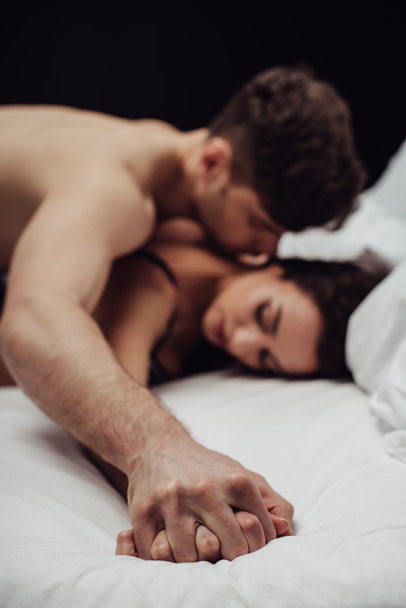 giovane coppia sdraiata a letto e tenendo le mani isolate sul nero
 - Foto, immagini