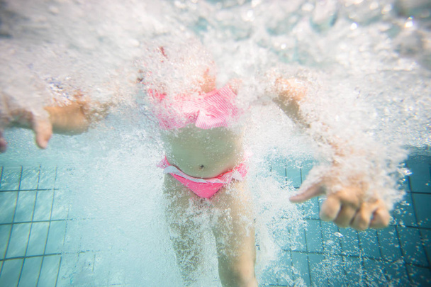 Wide angle underwater photo of a toddler girl swimming in a big swimming pool with goggles and a pink bikini - Foto, afbeelding