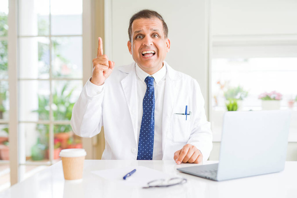 Středním věku lékař muž na sobě bílý lékařský plášť pracovat s notebookem na klinice ukazováčkem úspěšný nápad. Byl ukončen a šťastný. Číslo jedna. - Fotografie, Obrázek