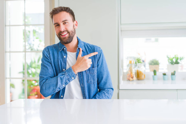 Handsome man at home cheerful with a smile of face pointing with hand and finger up to the side with happy and natural expression on face - Photo, Image