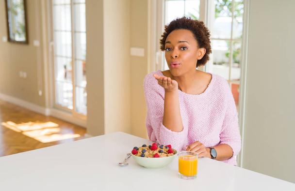 Mladá africká americká žena s zdravou snídani ráno doma při pohledu na fotoaparát Naznačení polibku s rukou na vzduchu jsou krásné a sexy. Láska výraz. - Fotografie, Obrázek