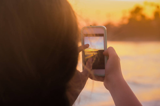 Молодая женщина делает пляж Сансет фото со смартфона
 - Фото, изображение