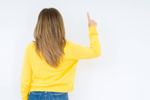 分離の上黄色のセーターを着ている美しい中年女性背景指手の背後後方を指すポーズ - 写真・画像