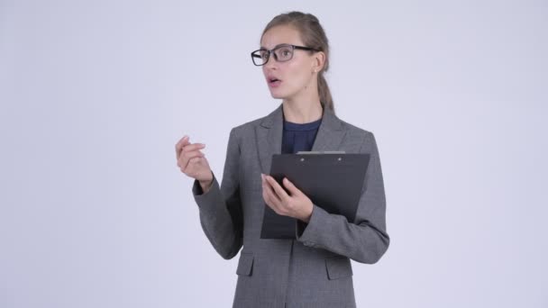 Young beautiful businesswoman talking while holding clipboard - Felvétel, videó