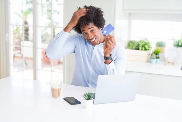 African American man met behulp van laptop en online winkelen met credit card benadrukt met de hand op het hoofd, geschokt met schaamte en verrassing gezicht, boos en gefrustreerd. Angst en boos voor fout. - Foto, afbeelding