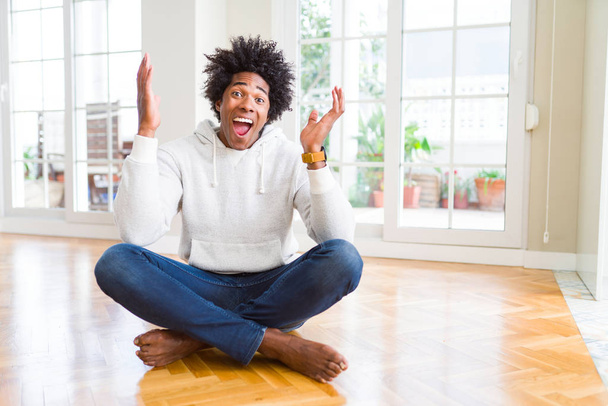 Afrikai amerikai férfi ült a földön otthon ünnepli, őrült és őrült siker karokkal emelt és zárt szemek sikoltozik izgatott. Győztes koncepció - Fotó, kép