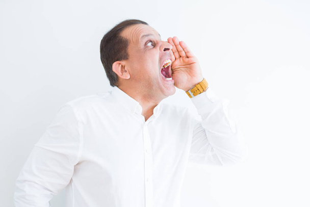 Mann mittleren Alters schreit verrückt mit den Händen über dem Mund über weißen w - Foto, Bild