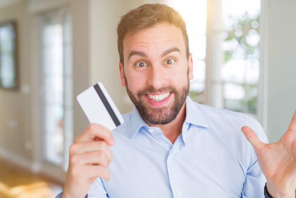 Красивый бизнесмен держит кредитную карту очень счастливый и взволнованный, победитель выражение празднования победы кричать с большой улыбкой и поднятые руки
 - Фото, изображение