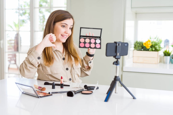 Bella giovane influencer donna registrazione make up video tutorial con faccia a sorpresa puntando il dito verso se stesso
 - Foto, immagini