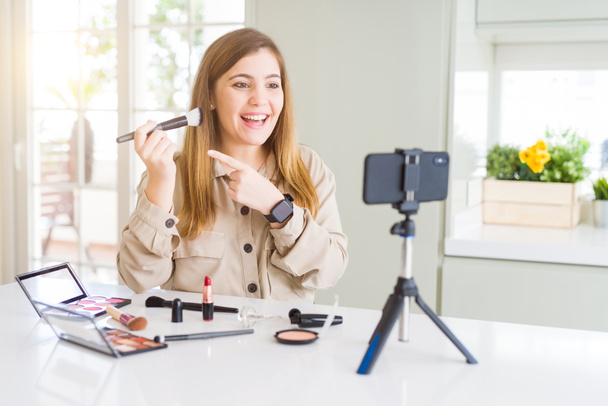Belle jeune femme influenceuse enregistrement maquillage tutoriel vidéo très heureux pointage avec la main et le doigt
 - Photo, image