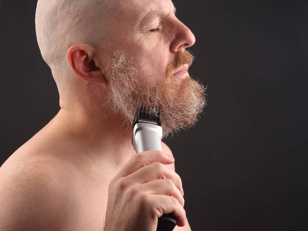 Бородатий чоловік з тримером для регулювання бороди в руці
 - Фото, зображення