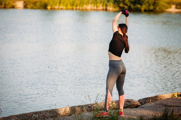 young athletic woman doing exercise side bend in Park near lake  - Photo, Image