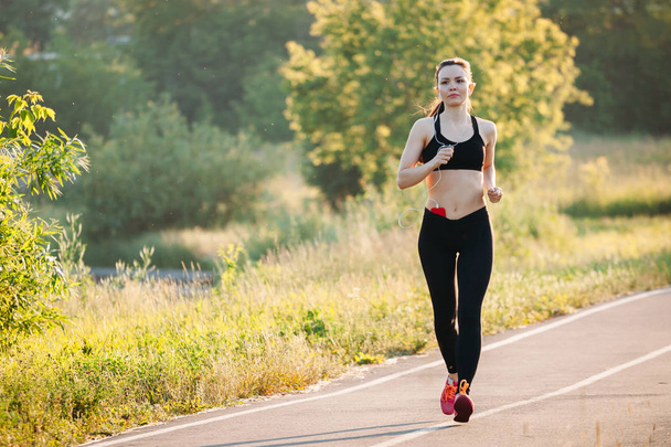 beautiful young sporty woman running on asphalt road in Park in  - Fotografie, Obrázek