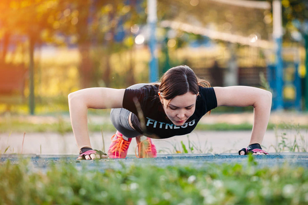 Beautiful slim brunette doing some Push-Ups outside in Park. Fit - Фото, изображение