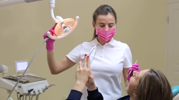 Портрет пациента к стоматологу для обследования и чистки зубов. Стоматолог проверяет зубы молодой женщины с помощью зеркала. - Кадры, видео