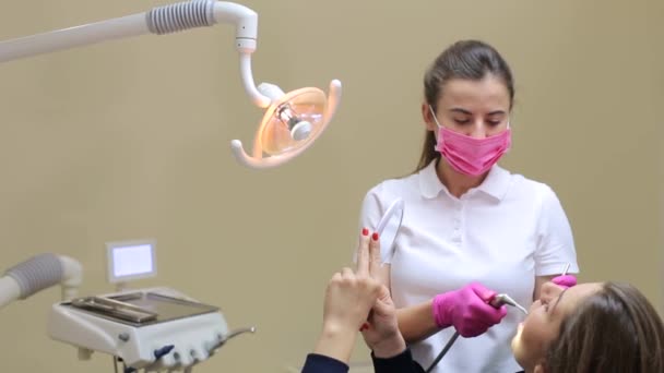 Портрет пацієнта стоматолога для перевірки та чистки зубів. Стоматолог перевіряє зуби молодої жінки з дзеркалом
. - Кадри, відео